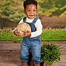 Icelee joined the competition — help win amazing prizes! brown_shoes, casual_clothing, child, curly_hair, cute, denim_overalls, green_plant, happy, indoor, natural_background, person, portrait, potted_plant, smiling, standing, studio_photo, toddler, wooden_floor, woven_ball, young_child