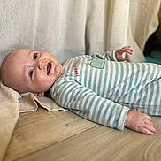 Timaël participe au concours pour gagner de l'argent avec cette photo : baby, infant, smile, drool, striped_onesie, wooden_floor, beige_fabric, happy, lying_down, child, cute, portrait, skin, hand, head, face, clothing, indoors, young, relaxed