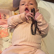 Bella joined the competition — help win amazing prizes! baby, infant, glasses, pink_clothing, bottle, bed, pillow, blanket, hand, face, person, indoor, soft_lighting, curious, cute, child, newborn, clothing, lying_down, home