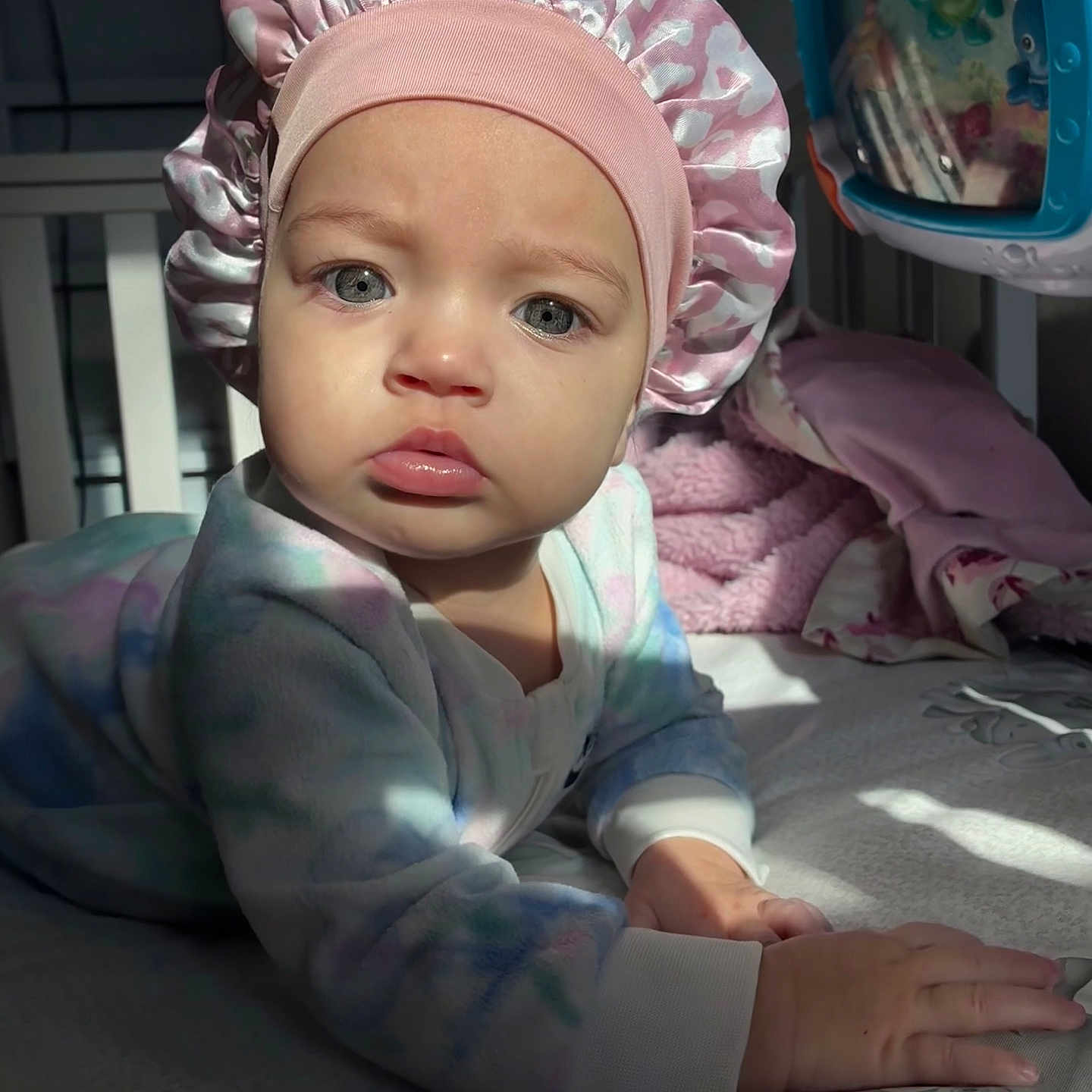 Maze joined the competition — help win amazing prizes! baby, infant, child, face, blue_eyes, pink_bonnet, onesie, bed, blanket, toy, indoor, soft_light, curious, hands, crawling, pastel_colors, cozy, portrait, young_child, expression