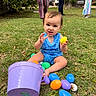 William is registered to the contest to win money with this photo: baby, child, easter_eggs, purple_bucket, grass, outdoor, people, trees, greenery, playing, summer_clothing, smiling, happy, blue_onesie, colorful, daylight, nature, celebration, fun, park