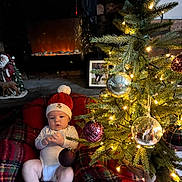 Cooper joined the competition — help win amazing prizes! baby, infant, christmas_tree, christmas_lights, ornaments, plaid_blanket, fireplace, holiday_decor, red_hat, red_booties, cozy, indoors, festive, holiday, cute, child, winter, celebration, sitting, decorations