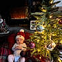 baby, infant, christmas_tree, christmas_lights, ornaments, plaid_blanket, fireplace, holiday_decor, red_hat, red_booties, cozy, indoors, festive, holiday, cute, child, winter, celebration, sitting, decorations