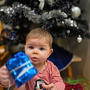 Victoria participe au concours pour gagner de l'argent avec cette photo : baby, blue_wrapping, celebration, child, christmas_tree, cute, face, festive, gift, hand, holiday, holiday_decor, indoor, ornaments, penguin_graphic, person, pink_shirt, present, silver_bow, smiling
