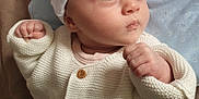 Deborah-Ema participe au concours pour gagner de l'argent avec cette photo : baby, infant, knit_sweater, white_clothing, cap, blue_background, star_pattern, fist, curious_expression, face, portrait, person, child, cute, indoors, soft_light, newborn, apparel, headwear, closeup