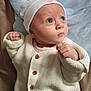 baby, infant, knit_sweater, white_clothing, cap, blue_background, star_pattern, fist, curious_expression, face, portrait, person, child, cute, indoors, soft_light, newborn, apparel, headwear, closeup