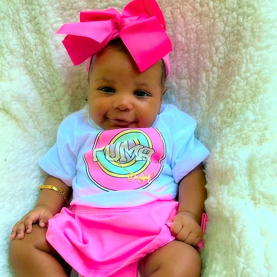 Deliyah joined the competition — help win amazing prizes! accessory, baby, blanket, bracelet, child, cute, fashion, footwear, hand, happy, headband, indoors, infant, pink_bow, pink_skirt, portrait, sitting, skin, smile, white_shirt