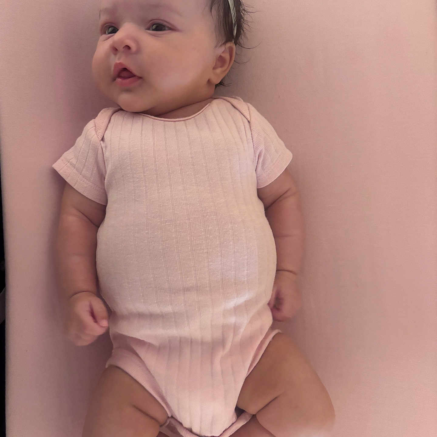 Emilia joined the competition — help win amazing prizes! baby, infant, onesie, headband, flower, pink, lying_down, cute, chubby, skin, child, young, adorable, soft_texture, portrait, person, newborn, expression, indoors, peaceful