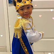 Sir Messiah is registered to the contest to win money with this photo: child, crown, costume, cape, blue, gold, smile, indoor, door, curly_hair, playful, portrait, young, person, floor, sign, white, fringe, gold_trim, happy