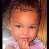 Princess Leilani is registered to the contest to win money with this photo: child, toddler, face, curly_hair, finger_in_mouth, purple_clothing, colorful_straps, cute, portrait, indoor, young_child, skin, person, baby, smile, expression, hair_tied_up, light, background, closeup