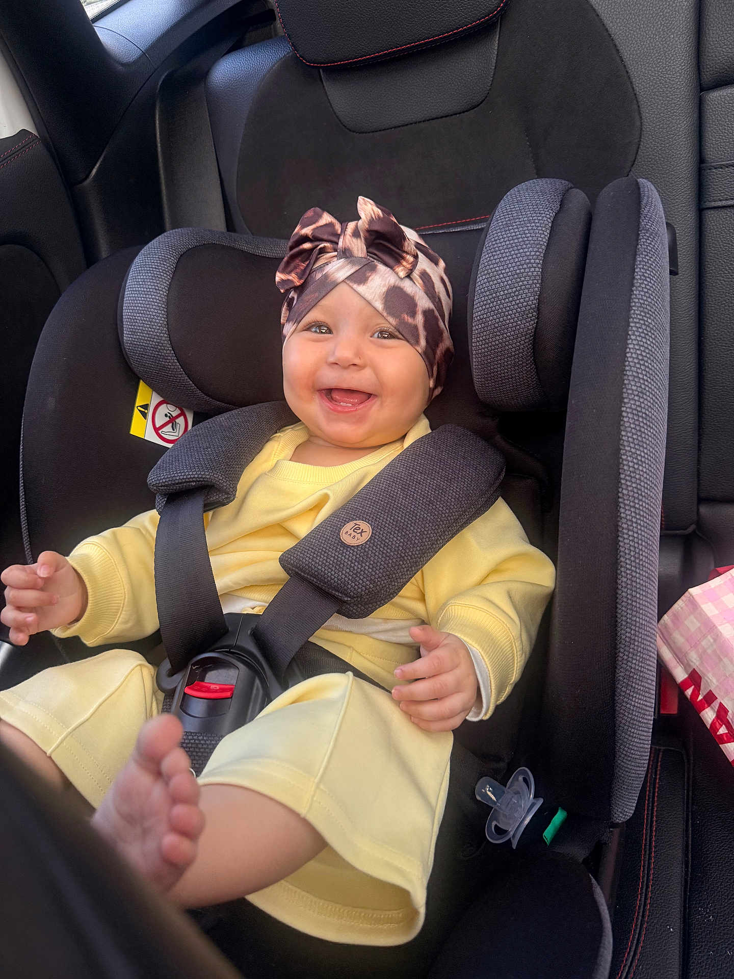 Alya participe au concours pour gagner de l'argent avec cette photo : baby, infant, child, smiling, car_seat, seat_belt, headwrap, bow, yellow_outfit, pacifier, cheek, hands, feet, car_interior, upholstery, safety_harness, portrait, happy, cute, seat_padding