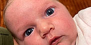 Maria a rejoint le concours — aidez-le/la à gagner de superbes lots ! baby, close_up, face, blue_eyes, infant, skin, expression, curious, soft_texture, clothing, newborn, portrait, head, couch, background, indoor, person, young_child, cozy, warm