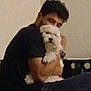 Rita is registered to the contest to win money with this photo: person, dog, hugging, indoor, fluffy_dog, black_clothing, white_dog, seated, affection, love, pet, home, wall, chair, casual, short_hair, closeup, cuddling, animal, companion