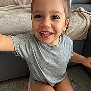 Djoulyna a rejoint le concours — aidez-le/la à gagner de superbes lots ! blanket, carpet, child, clothing, cute, face, grey_shirt, hair_tied, happy, home, indoors, joy, person, playful, shorts, sitting, smiling, sofa, toddler, young