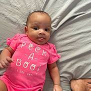 Skyler joined the competition — help win amazing prizes! baby, infant, pink_clothing, onesie, lying_down, bed, gray_bedspread, tongue_out, tattoo, arm, hand, cute, playful, child, person, indoors, fabric, wrinkles, skin, casual