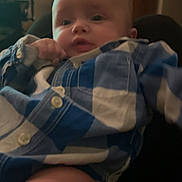 Lorenzo is registered to the contest to win money with this photo: baby, child, infant, portrait, face, eyes, curious, indoor, sitting, blue_outfit, plaid, clothing, hand, knee, chair, living_room, bookshelf, home, candid, photograph