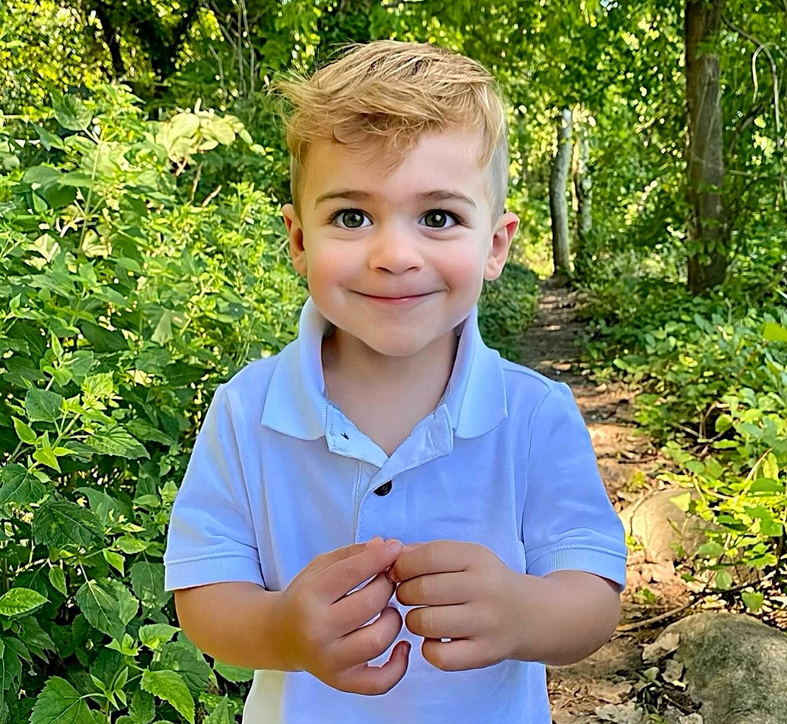 Bradley is registered to the contest to win money with this photo: baby_toddler_clothing, child, electric_blue, fun, gesture, grass, grass_family, happy, iris, joy, people_in_nature, person, plant, sitting, sleeve, smile, standing, t_shirt, terrestrial_plant, thumb