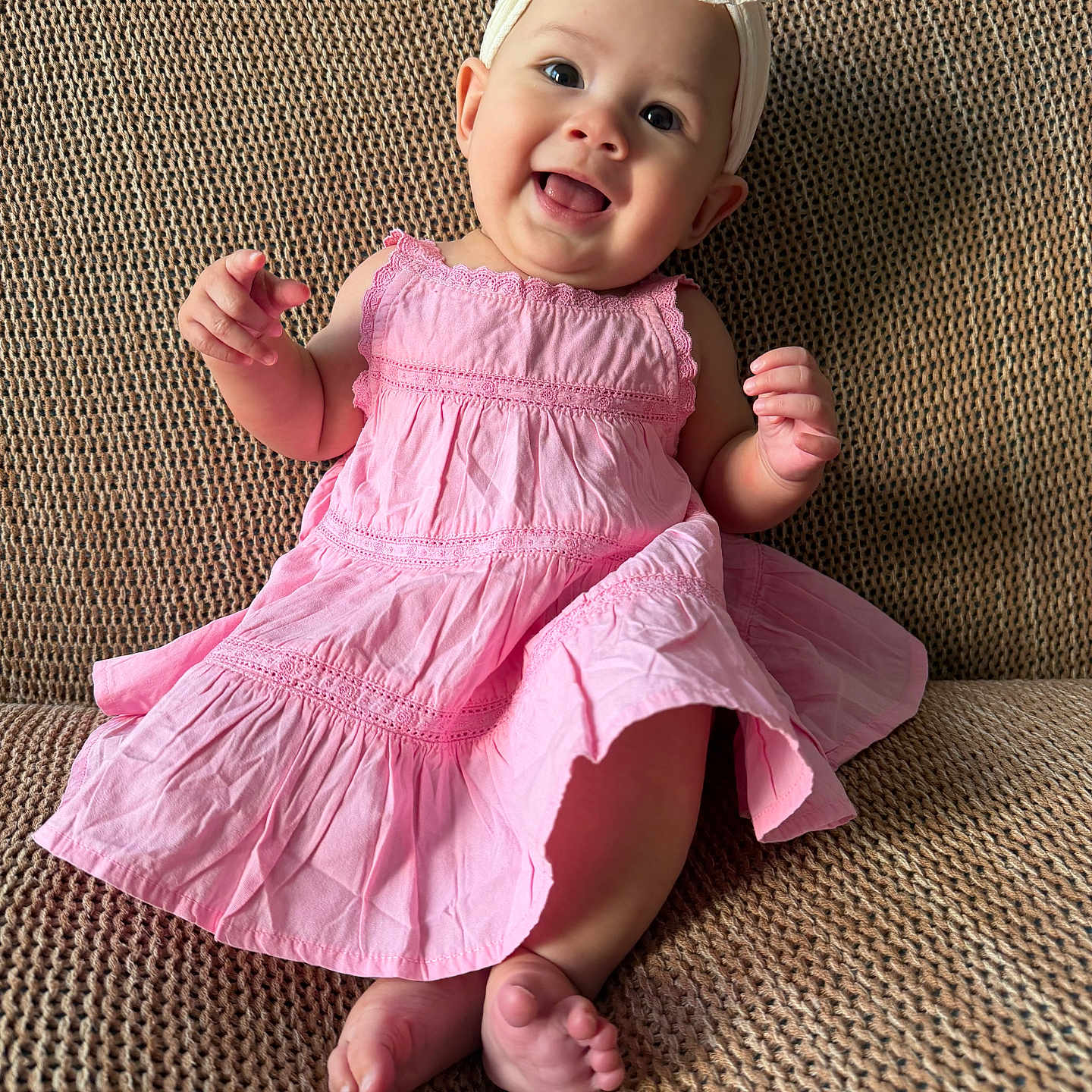 Mai is registered to the contest to win money with this photo: baby, child, smile, pink_dress, headband, bow, couch, textured_fabric, happy, cute, infant, sitting, indoors, portrait, skin, feet, hand, bright, eyes, clothing