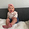 baby, child, infant, headband, pink_bow, smiling, happy, sitting, mattress, foot, clothing, long_sleeve, shorts, indoor, wall, couch, texture, person, cute, playful