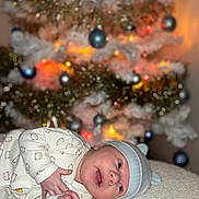 Tylio a rejoint le concours — aidez-le/la à gagner de superbes lots ! baby, child, christmas_tree, cute, decorations, face, festive, happy, hat, holiday, indoors, infant, lying_down, newborn, onesie, ornaments, portrait, smile, soft_surface, warm_lighting