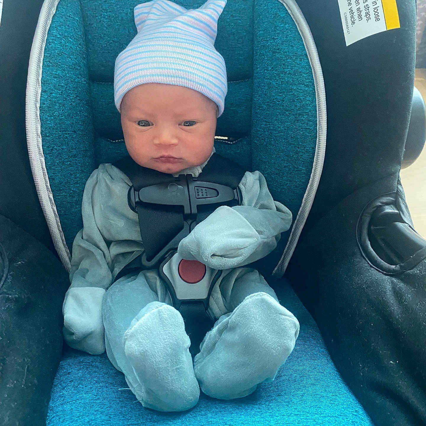 Jayden is registered to the contest to win money with this photo: baby, beanie, blue_clothing, car_seat, child, cute, headwear, indoor, infant, newborn, pajamas, person, portrait, safety, seat, serious_face, sitting, small, straps, young