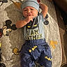 baby, infant, child, portrait, lying_down, superhero, batman, costume, beanie, blue_clothing, mickey_mouse, blanket, indoor, cozy, smiling, face, hands, text_on_clothing, soft_lighting, photography
