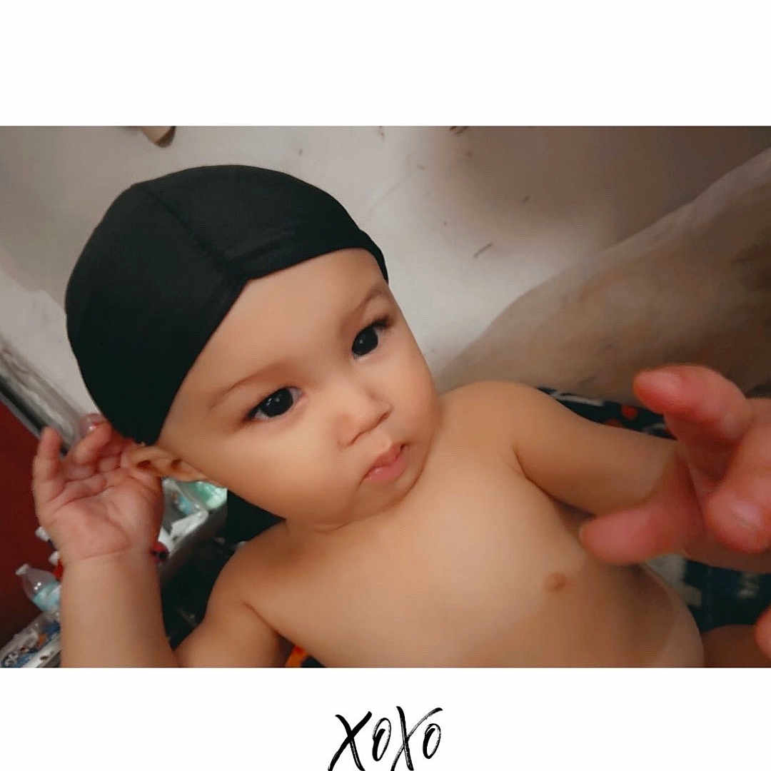 Kylo joined the competition — help win amazing prizes! baby, infant, child, portrait, black_cap, lying_down, bare_chested, face, eyes, serious_expression, curious, adult_hand, indoor, bed, blanket, photograph, handwritten_text, xoxo, close_up, family