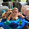 baby, child, infant, activity_walker, toy, indoor, living_room, armchair, blanket, blue, sitting, face, portrait, wide_eyed, curious, floor, window, daylight, household, playtime