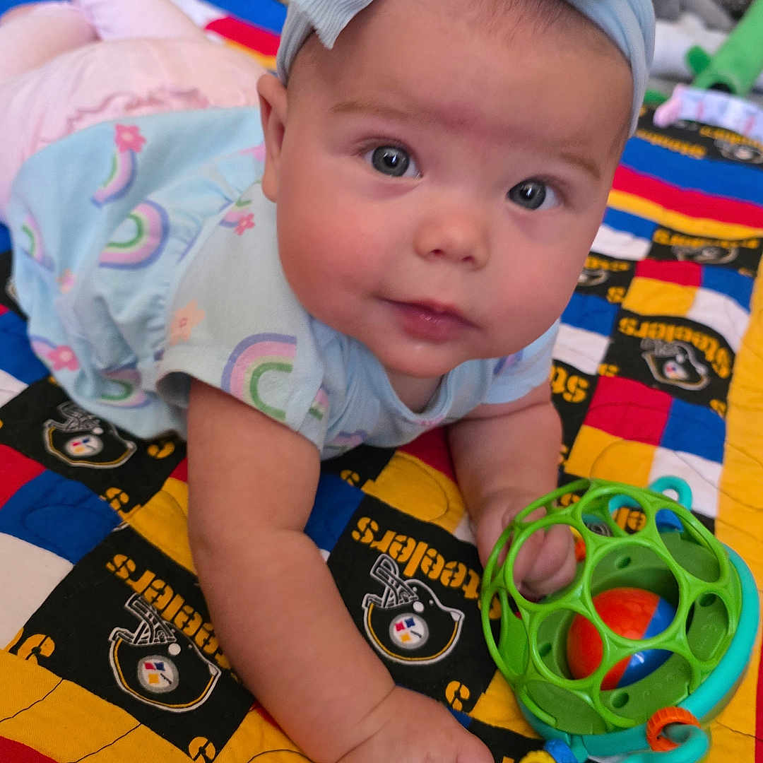 Journey is registered to the contest to win money with this photo: baby, blue, child, clothing, colorful, crawling, cute, face, floor, hand, headband, indoor, infant, pattern, person, pink, playtime, quilt, soft_toys, toy