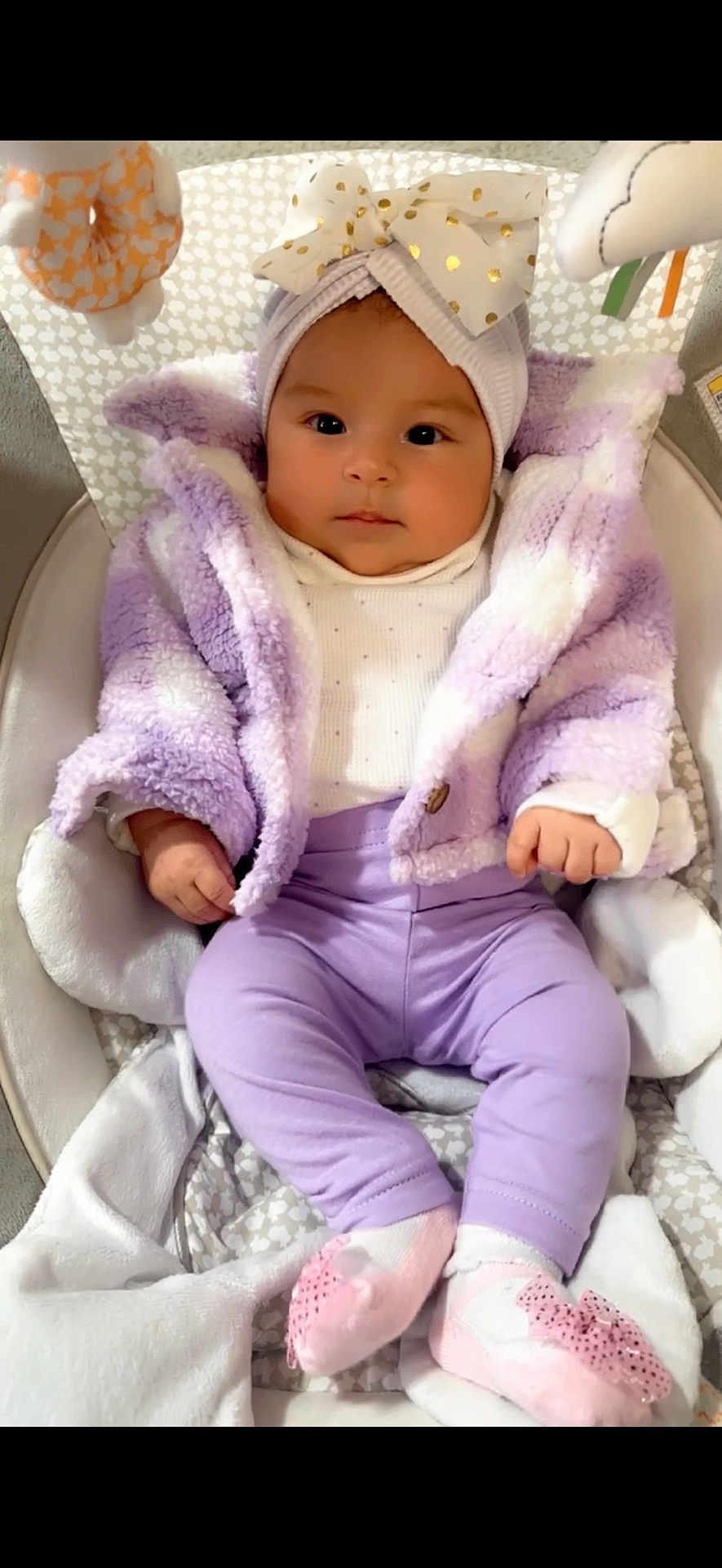 Ariana is registered to the contest to win money with this photo: baby, infant, child, headband, bow, purple_clothing, jacket, pants, pink_socks, baby_seat, soft_toys, cute, portrait, indoors, smiling, cozy, comfortable, face, hands, feet