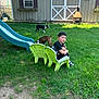 child, boy, green_chair, plush_toy, dog, slide, grass, backyard, shed, window, fence, outdoor, summer, daylight, toy, pet, play, welcome_sign, casual_clothing, nature