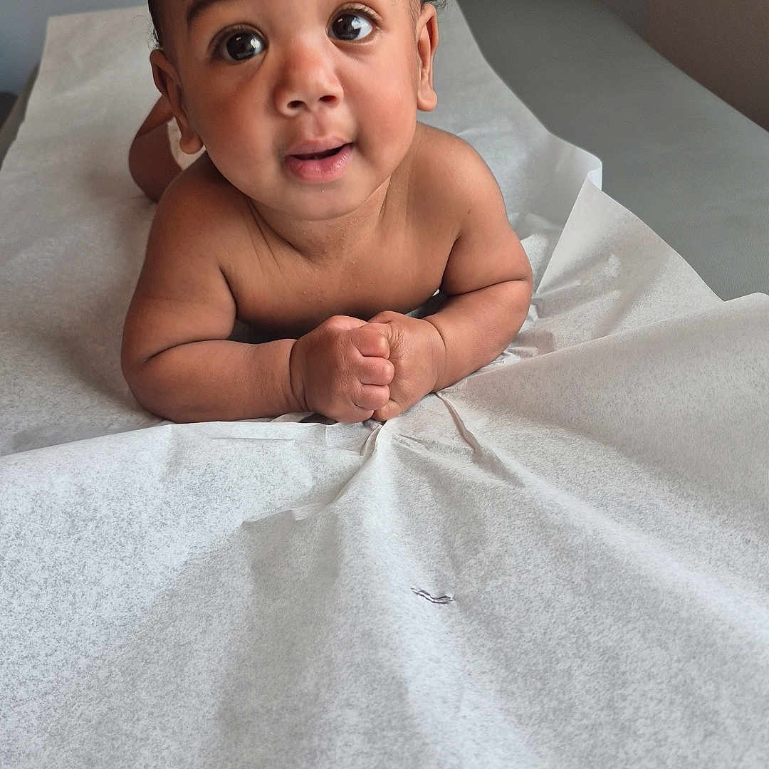 Ahisiah joined the competition — help win amazing prizes! baby, infant, curly_hair, big_eyes, medical_table, paper_cover, skin, child, cute, portrait, indoors, expression, hands, lying_down, young_child, looking_up, healthcare, examination, room, curiosity