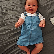 Alba participe au concours pour gagner de l'argent avec cette photo : baby, smiling, denim_dress, white_shirt, lying_down, gray_sheet, happy, infant, cute, portrait, child, skin, clothing, small_hands, feet, indoors, one_person, young_child, joyful, casual