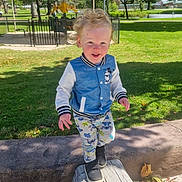 Finnegan is registered to the contest to win money with this photo: child, curly_hair, daylight, fence, grass, happy, jacket, leaves, log, mickey_mouse, nature, outdoor, pants, park, playground, shoes, smiling, sunny, toddler, trees
