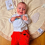 Abel a rejoint le concours — aidez-le/la à gagner de superbes lots ! baby, infant, smiling, happy, playmat, blanket, milestone_card, bunny_ears, red_pants, white_shirt, socks, hardwood_floor, portrait, rosy_cheeks, card, lying_down, cozy, cute, clothing, face
