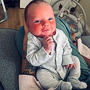 Bodhi joined the competition — help win amazing prizes! baby, infant, onesie, tattoo, hand, face, blue_eyes, smile, couch, blanket, home_interior, wood_floor, toy, person, sitting, cute, relaxing, portrait, human, indoor