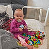baby, pacifier, toy, blanket, doll, car_toy, floor, purple_clothing, indoor, child, seat, playtime, cushion, table, living_room, person, cute, infant, colorful, soft_toys