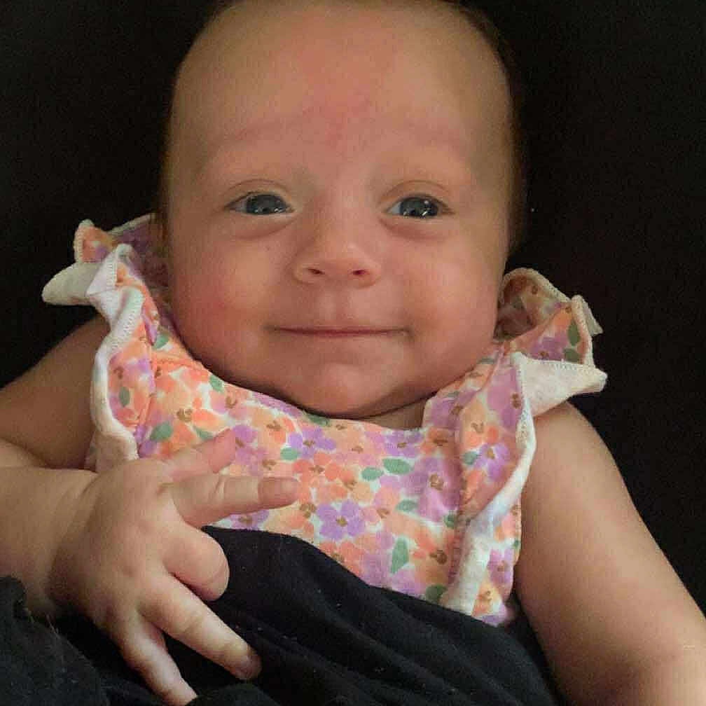 Freyja joined the competition — help win amazing prizes! arm, baby, blanket, child, clothing, cute, face, floral_dress, hand, happy, indoors, infant, peaceful, person, portrait, resting, sitting, skin, smile, young