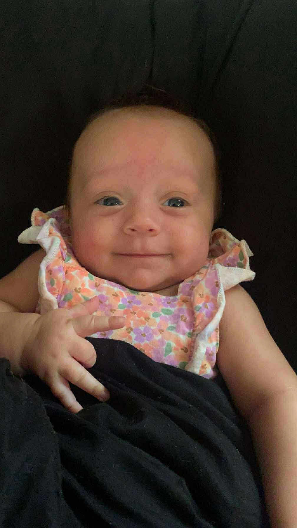 Freyja joined the competition — help win amazing prizes! baby, infant, smile, face, arm, hand, blanket, floral_dress, clothing, cute, child, young, portrait, skin, person, sitting, indoors, resting, happy, peaceful