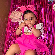 Leylani is registered to the contest to win money with this photo: baby, background, bracelet, celebration, chewing, child, cute, doll, dress, happy, headband, indoors, necklace, person, pink, playful, portrait, purse, ribbon, streamers
