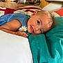 Camille participe au concours pour gagner de l'argent avec cette photo : toddler, child, smile, face, blue_dress, pillow, bed, indoor, cute, happy, skin, hair, flower_patch, lying_down, cozy, soft_light, person, young_child, portrait, expression