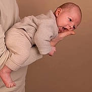 Neylo participe au concours pour gagner de l'argent avec cette photo : adult_hand, baby, beige_clothing, casual, child, cute, expression, foot, head, holding, infant, knitwear, person, playful, portrait, skin, soft_lighting, studio_photo, tongue_out, warm_background