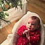 baby, infant, red_onesie, polka_dots, blanket, christmas_tree, tree_lights, holiday, indoors, wood_floor, cute, child, portrait, soft_texture, warm_lighting, seasonal, festive, toddler, face, expression