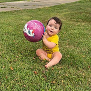 Christian joined the competition — help win amazing prizes! baby, child, grass, ball, outdoor, toy, playing, smiling, curly_hair, yellow_onesie, driveway, car, house, suburban, daytime, nature, greenery, happy, sitting, person