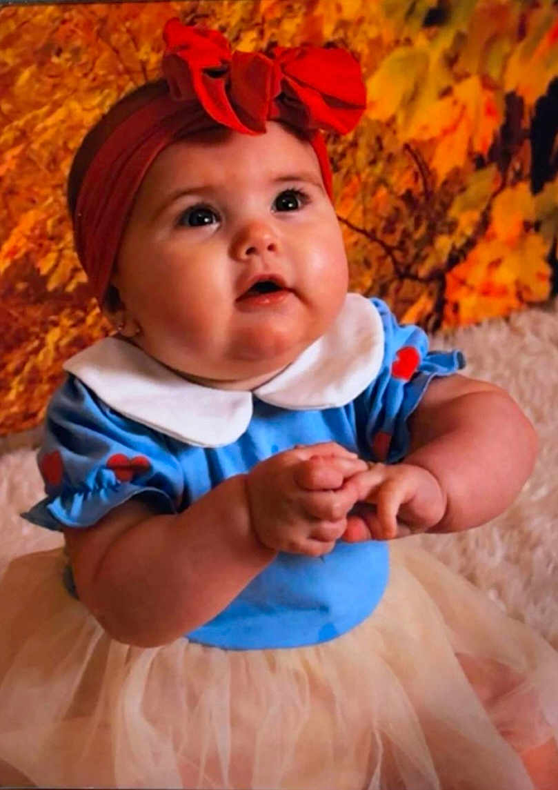 Isla-Grace is registered to the contest to win money with this photo: baby, child, toddler, blue_clothing, red_headband, bow, tutu, cute, portrait, indoors, autumn, leaves, background, chubby_cheeks, hands, expression, curious, sitting, young_child, face