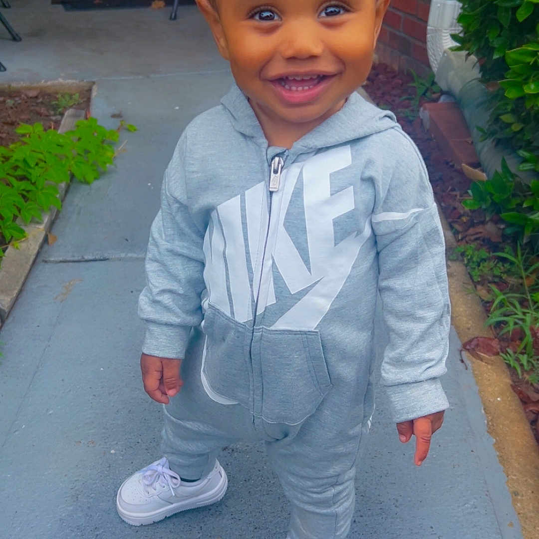 Chozyn joined the competition — help win amazing prizes! toddler, child, smiling, outdoor, sidewalk, nike, tracksuit, hoodie, white_sneakers, greenery, brick_wall, door, chair, happy, person, portrait, casual_wear, daylight, standing, cute