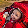baby, infant, child, red_bunting, stroller, hood, blanket, toy_plush, zipper, blue_eyes, smile, cheeks, cozy_clothing, outdoor, park, sunlight, portrait, warm_jacket, happy, soft_focus