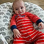 baby, infant, child, onesie, red_clothing, striped_clothing, elephant_pattern, cushion, smile, face, hand, floor, wood_flooring, comfort, indoor, portrait, young_child, sitting, cute, happy