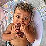baby, child, infant, curly_hair, baby_seat, meat, chewing, toy, colorful, pattern, cushion, cute, hands, face, skin, expression, sitting, indoors, closeup, young
