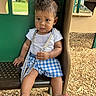 Haze is registered to the contest to win money with this photo: toddler, child, playground, outdoor, wood_chips, green_panel, blue_shorts, white_shirt, barefoot, curly_hair, sitting, play_area, daylight, young_child, casual_clothing, thoughtful_expression, summer, park, person, play_equipment